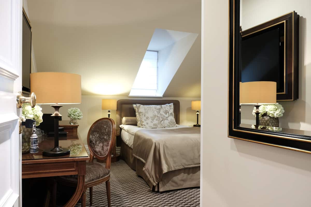 Habitación de hotel con cama, escritorio, silla, lámpara y espejo.
