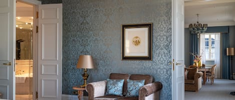 Una habitación con papel tapiz estampado, un cuadro en la pared, un sofá con cojines, una lámpara y una cama.