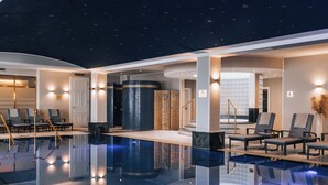 Un espace piscine intérieur moderne, avec une eau cristalline, des sièges disposés autour de la piscine et un plafond étoilé.