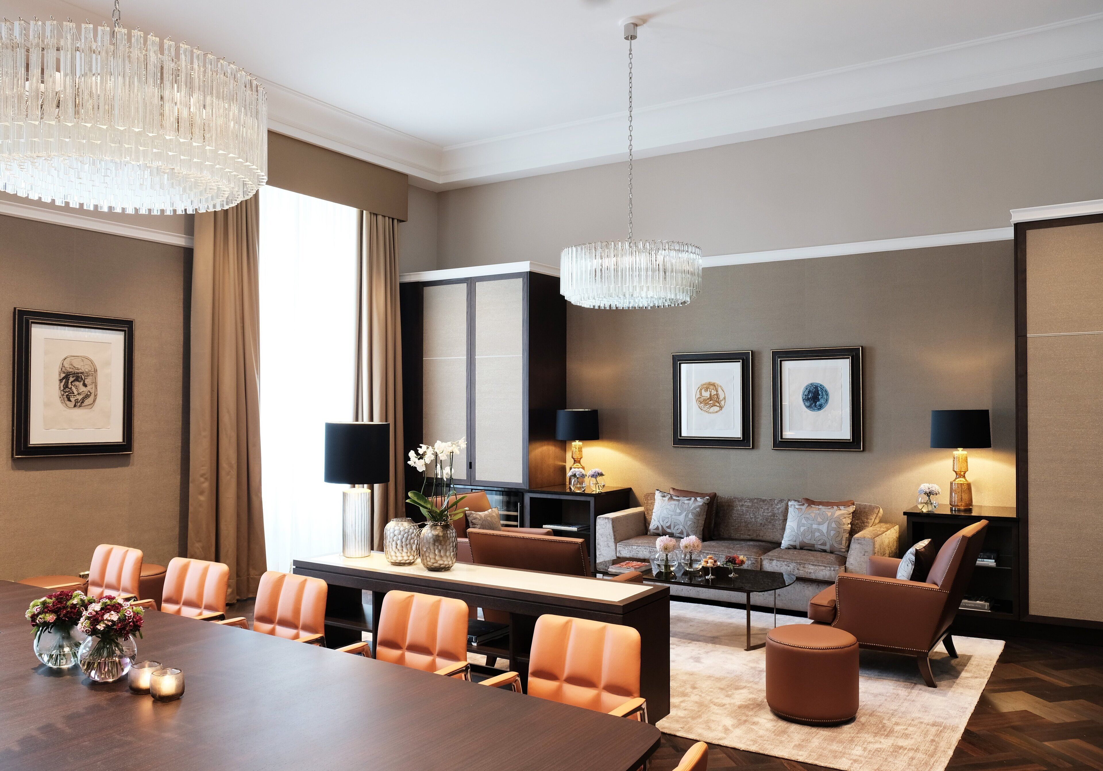 A modern hotel room with a dining area, a sofa set, and a chandelier.