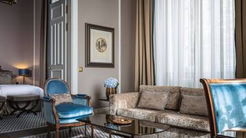 Ein Hotelzimmer mit einem Bett, einem blauen Sessel, einer gemusterten Couch, einem kleinen Tisch und einem gerahmten Bild an der Wand.