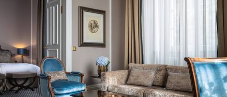 A hotel room with a bed, a blue armchair, a patterned sofa, a small table, and a framed picture on the wall.