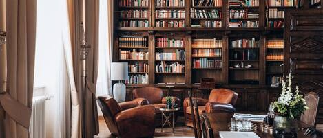 Una biblioteca con estanterías, sillones de cuero, una mesa de centro y un jarrón con flores.
