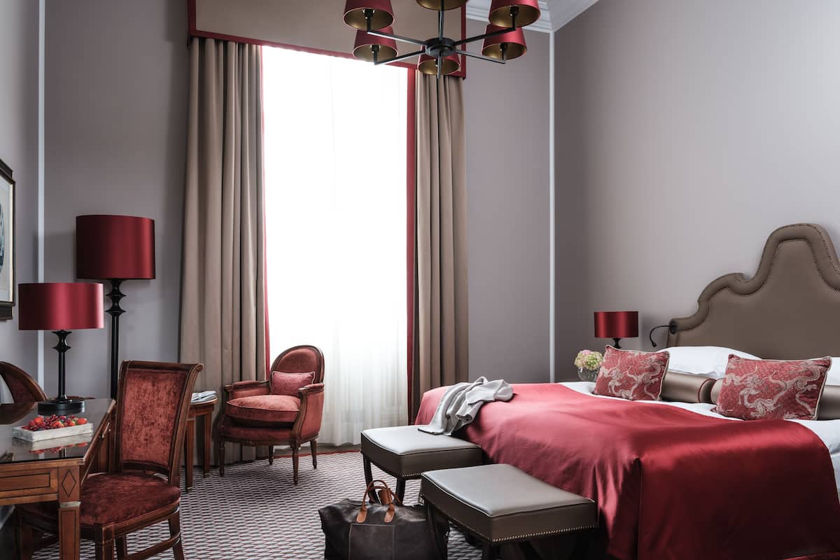Habitación de hotel con cama, escritorio, silla, lámpara y ventana con cortinas.