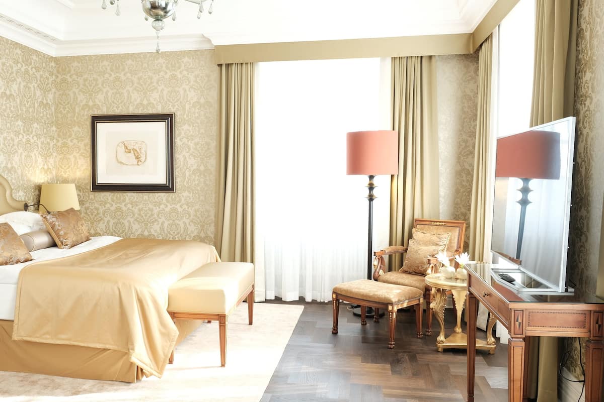 Un espacioso dormitorio con una cama grande, una zona de estar con una silla y una mesa, y una televisión.