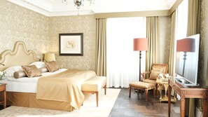 A spacious bedroom with a large bed, a sitting area with a chair and table, and a television.