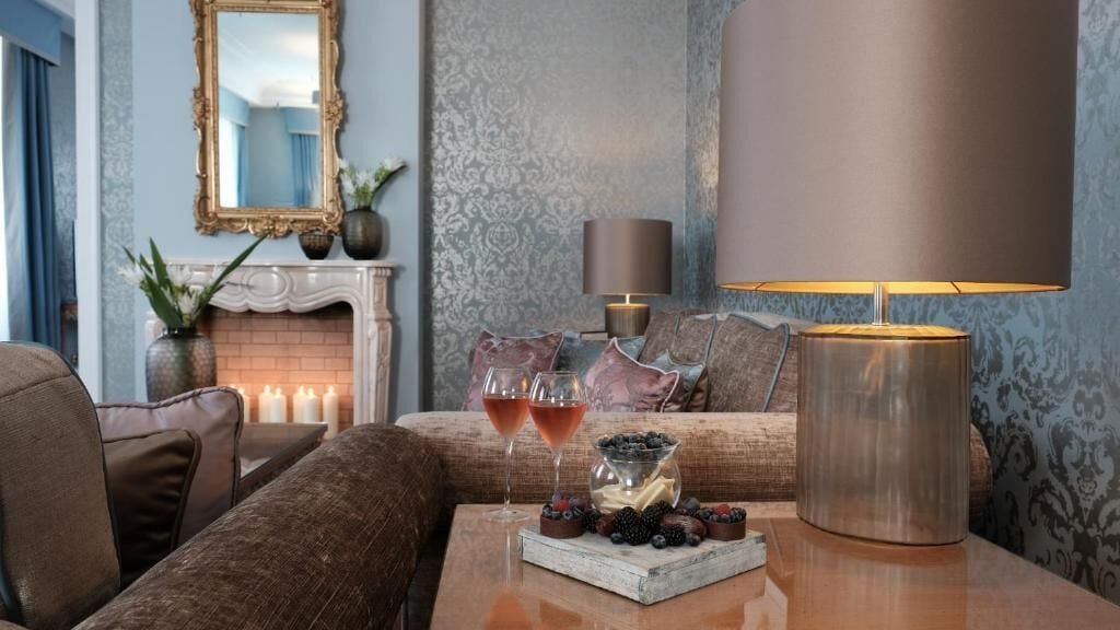 Ein gemütliches Wohnzimmer mit Kamin, einer Couch, einem Couchtisch mit einem Weinglas und Dessert sowie einer Lampe.