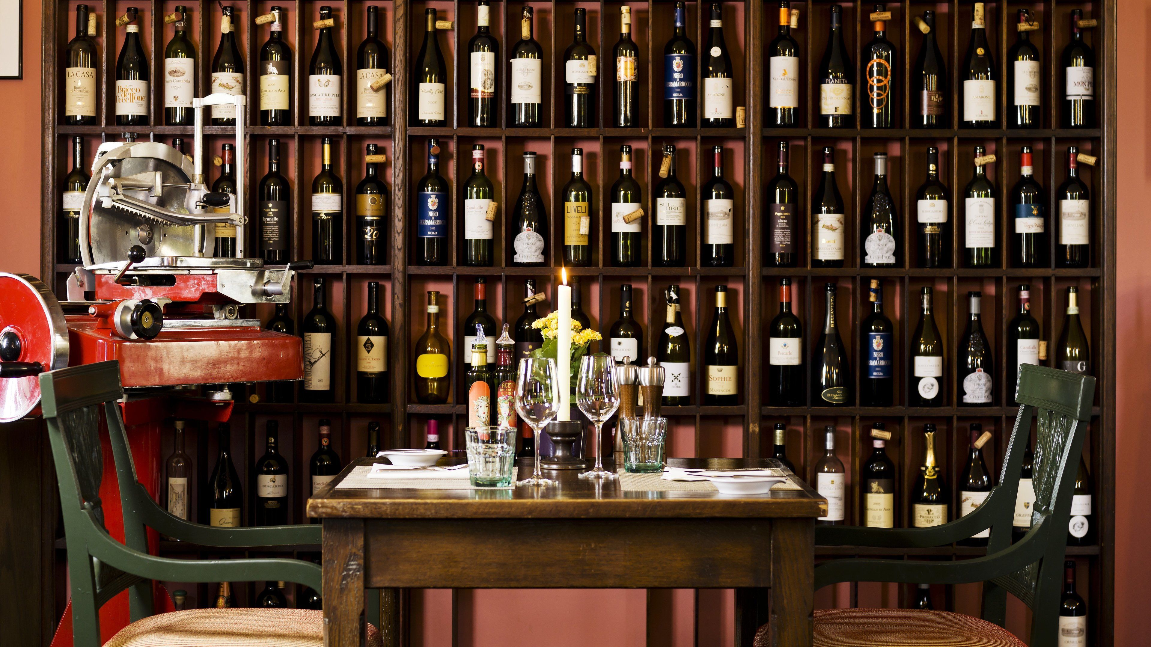 A wine cellar with numerous bottles on shelves and a table with glasses and a candle.