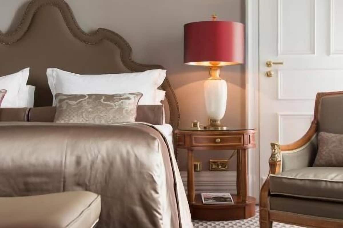 Una habitación de hotel con una cama grande, una mesita de noche con lámpara, una silla y un adorno en la pared.
