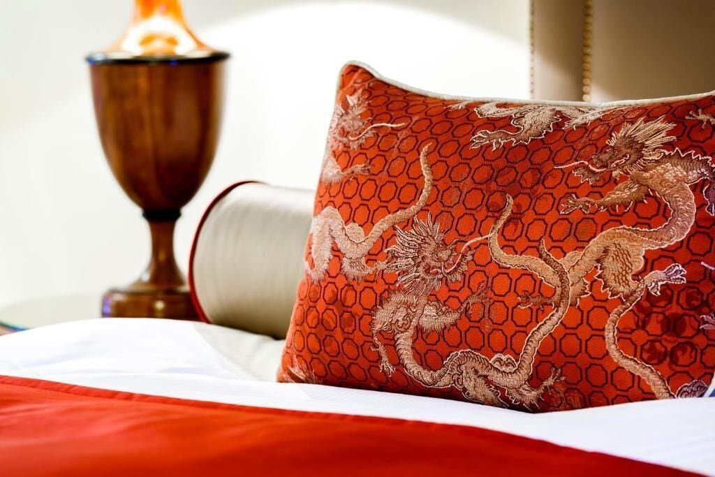 A bed with a red and white pillow featuring a dragon design, a wooden lamp, and a white headboard.