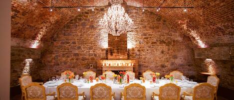A long dining table set for a meal in a room with brick walls and a high ceiling.