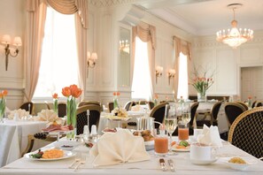 A formal dining room with tables set for breakfast, featuring a variety of dishes, drinks, and elegant table settings.