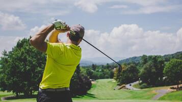Um campo de golfe com um jogador de camisa amarela e calças pretas, preparando-se para o movimento.