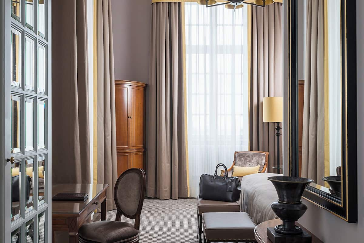 Habitación de hotel con cama, escritorio, silla, armario y un espejo grande.