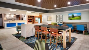 Un hall d’hôtel moderne comprenant un espace repas, une cuisine et un téléviseur diffusant des images d’un parcours de golf.