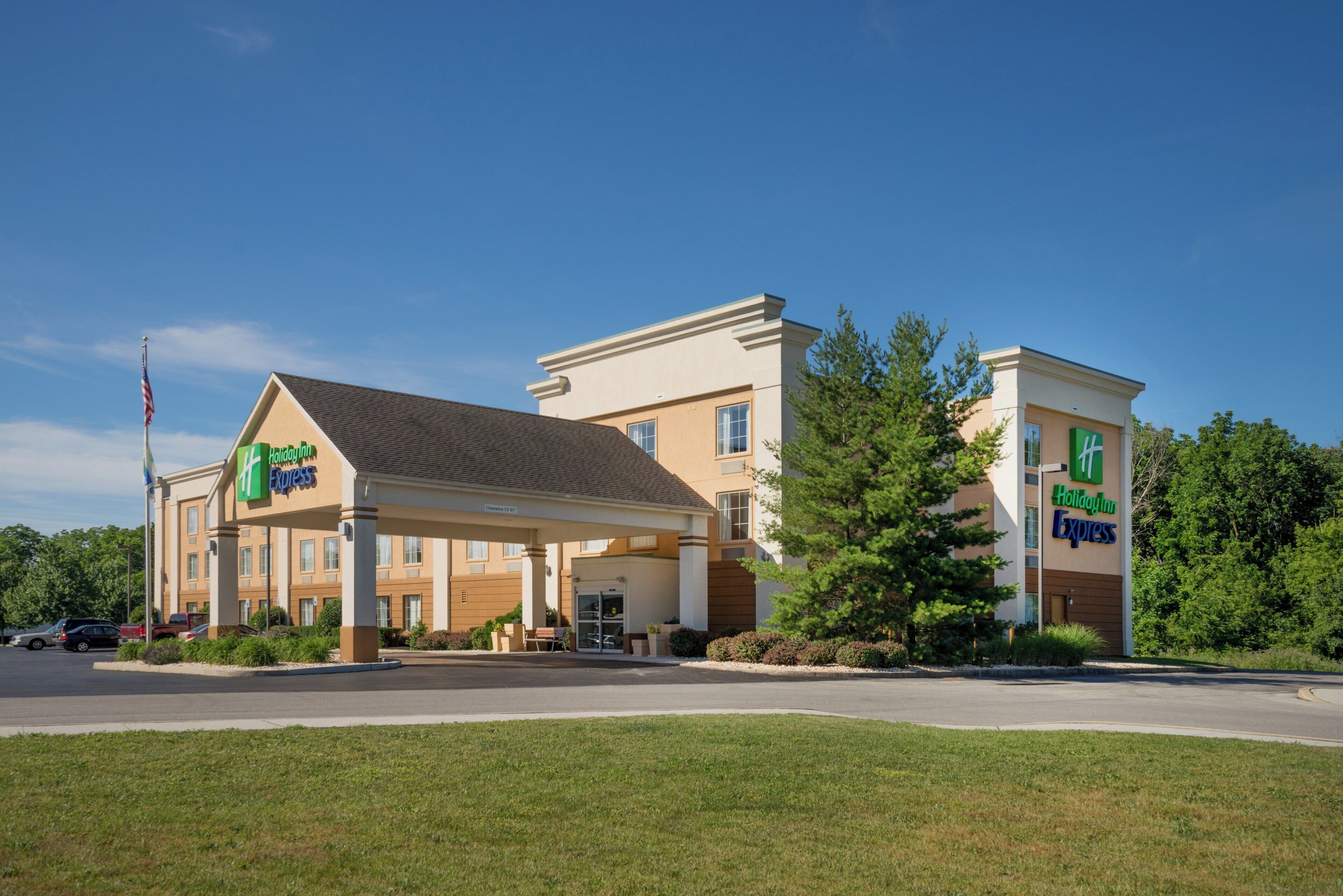 Un hotel Holiday Inn Express con entrada cubierta, una bandera y un estacionamiento.