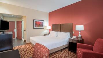 A hotel room with a large bed, two bedside tables with lamps, a desk with a computer, a TV, and a red armchair.