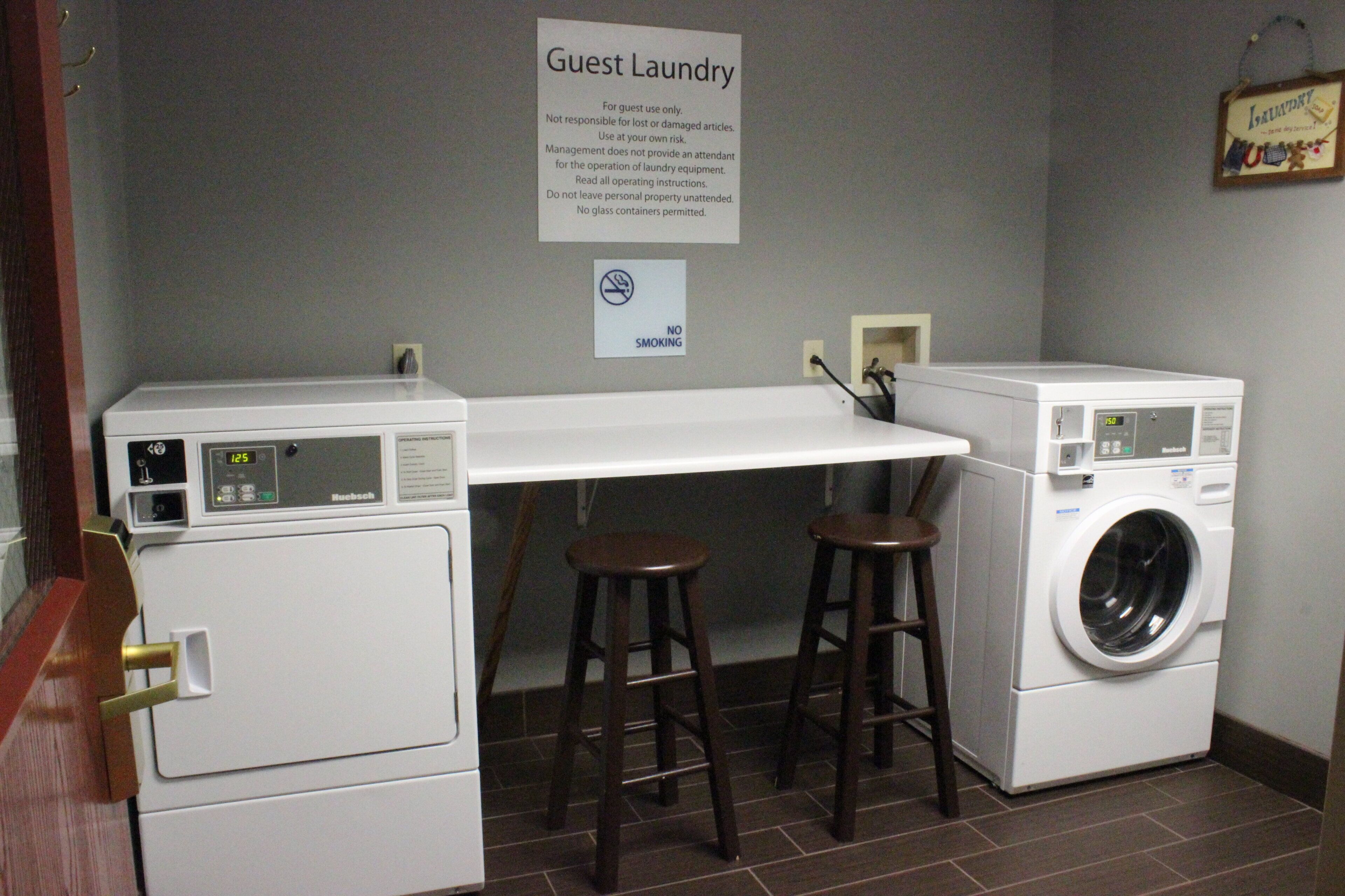 A guest laundry area with a sign, two washing machines, a dryer, and a table with stools.