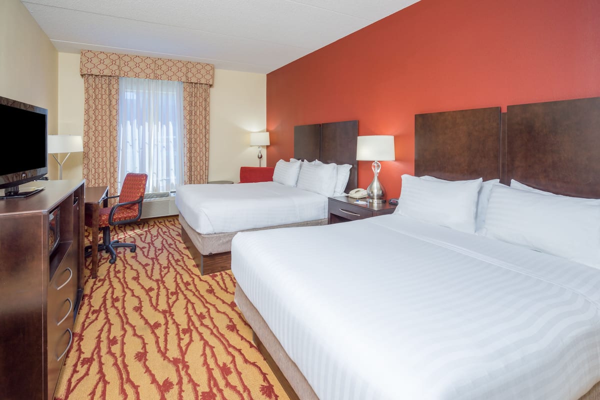 A hotel room with two beds, a desk with a TV, and a red carpeted floor.