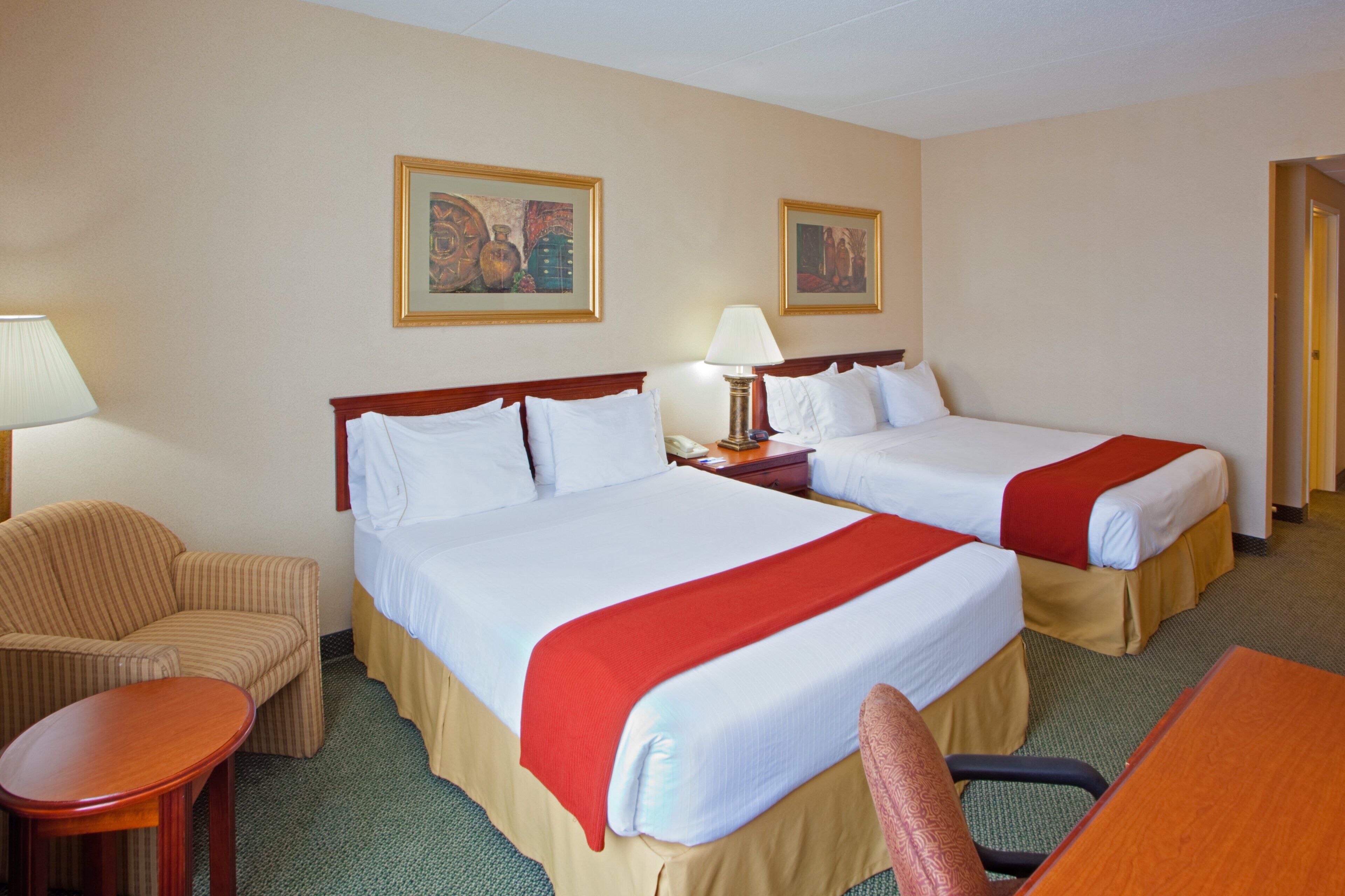 A hotel room with two beds, a chair, a desk, and two lamps.