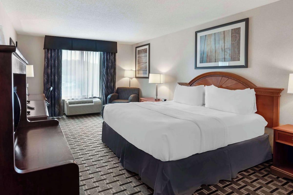 A hotel room with a large bed, a desk, a chair, and a window with curtains.