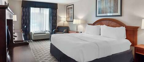 Una habitación de hotel con una cama grande, un escritorio, una silla y un ventanal con cortinas.