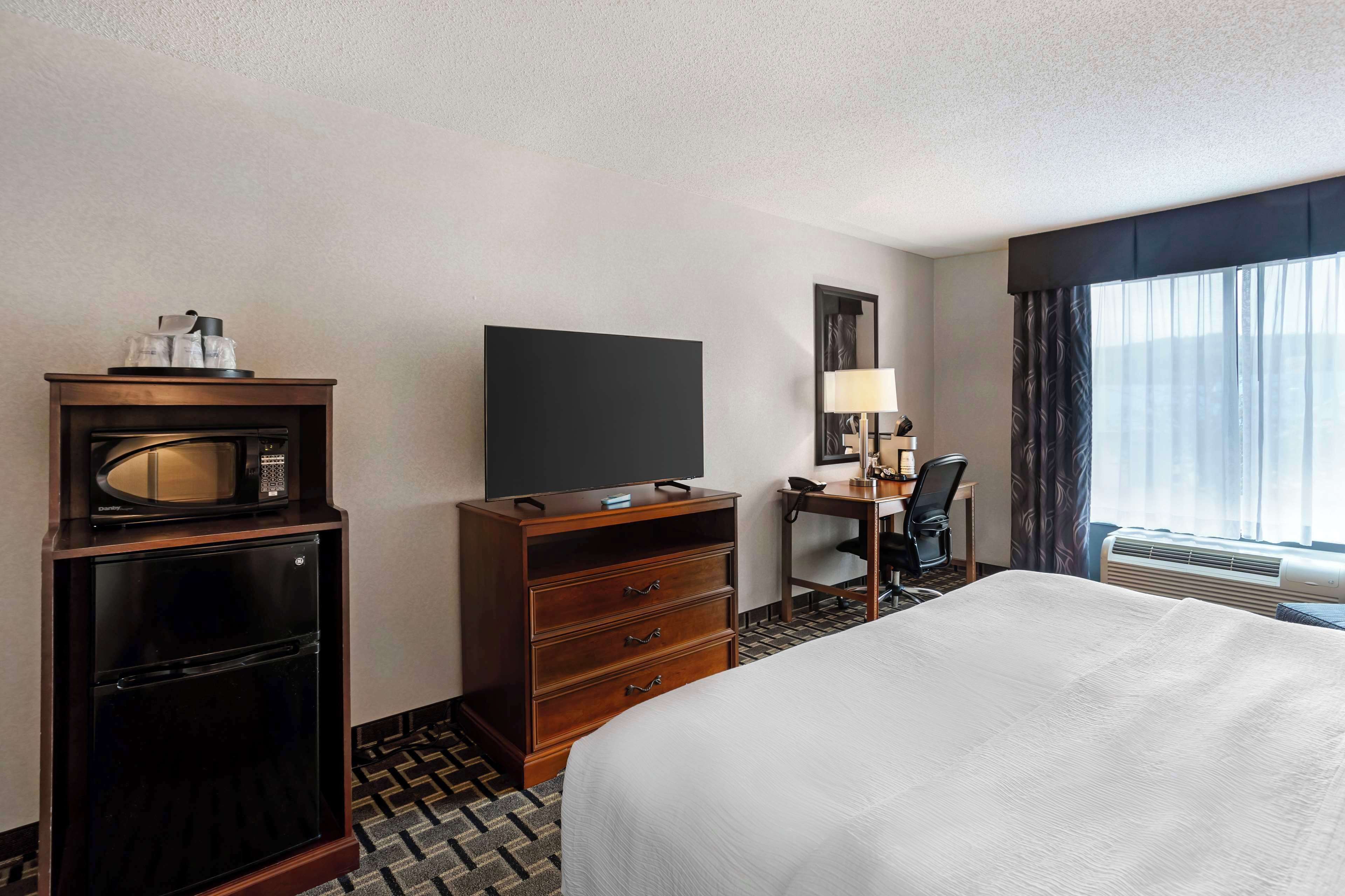 Una habitación de hotel con cama, escritorio, televisor, microondas y cómoda.