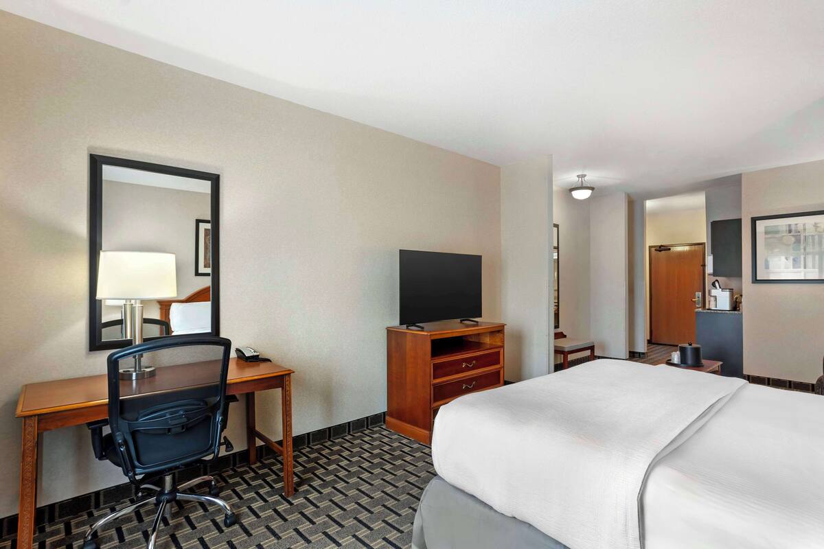 A hotel room with a bed, a desk with a chair, a television, and a mirror.