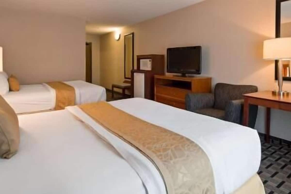 A hotel room with two beds, a desk, a chair, a television, and a lamp.