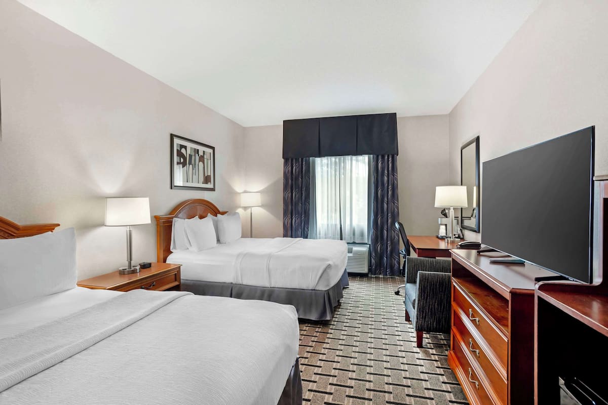 A hotel room with two beds, a desk with a TV, a dresser, and a window with curtains.