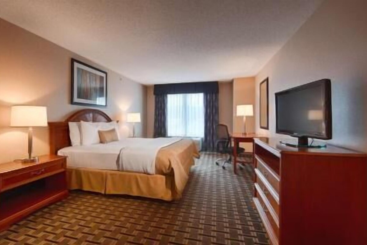 A hotel room with a bed, bedside tables, a TV, and a desk.