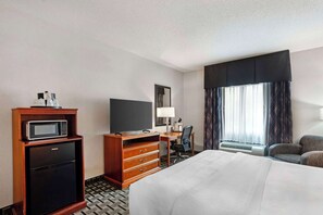 A hotel room with a bed, a desk with a chair, a minibar, a television, and a window with curtains.