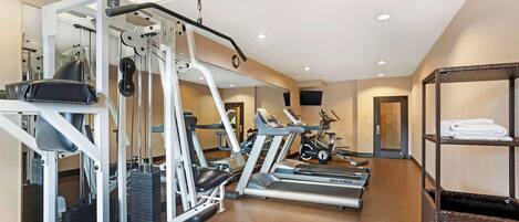 A hotel fitness center with cardio machines, weight training equipment, and a mirrored wall.