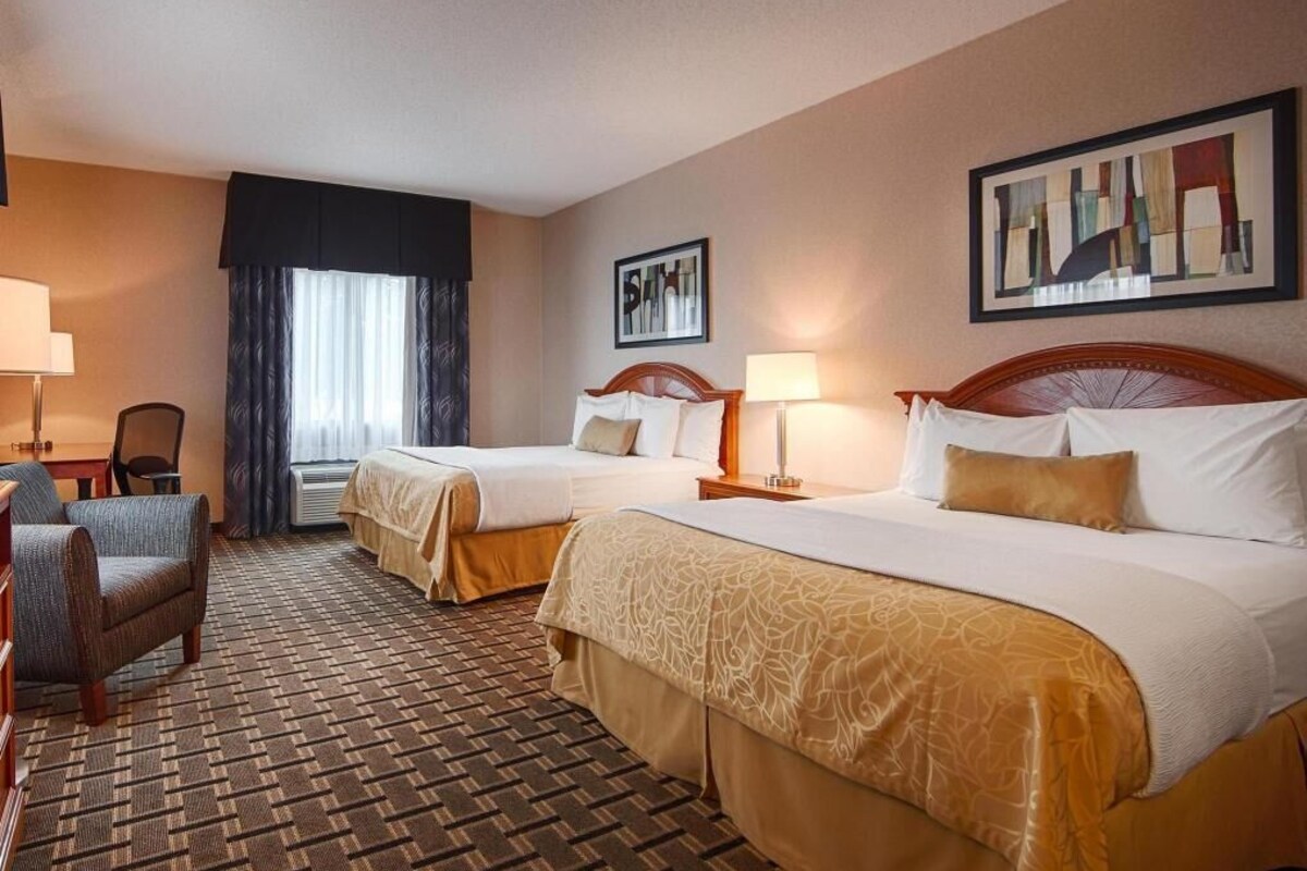 A hotel room with two beds, a desk, a chair, a lamp, and a framed picture on the wall.