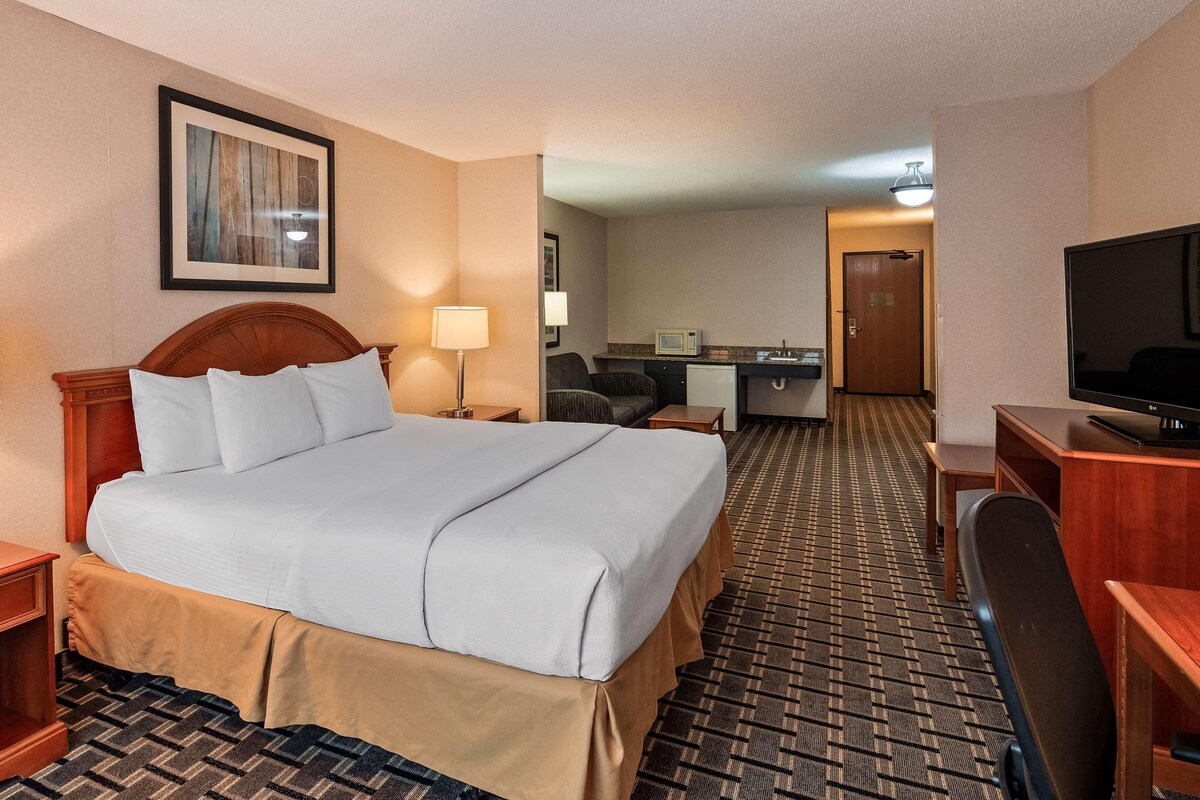 A hotel room with a bed, bedside tables, a desk, a chair, a television, and a microwave.