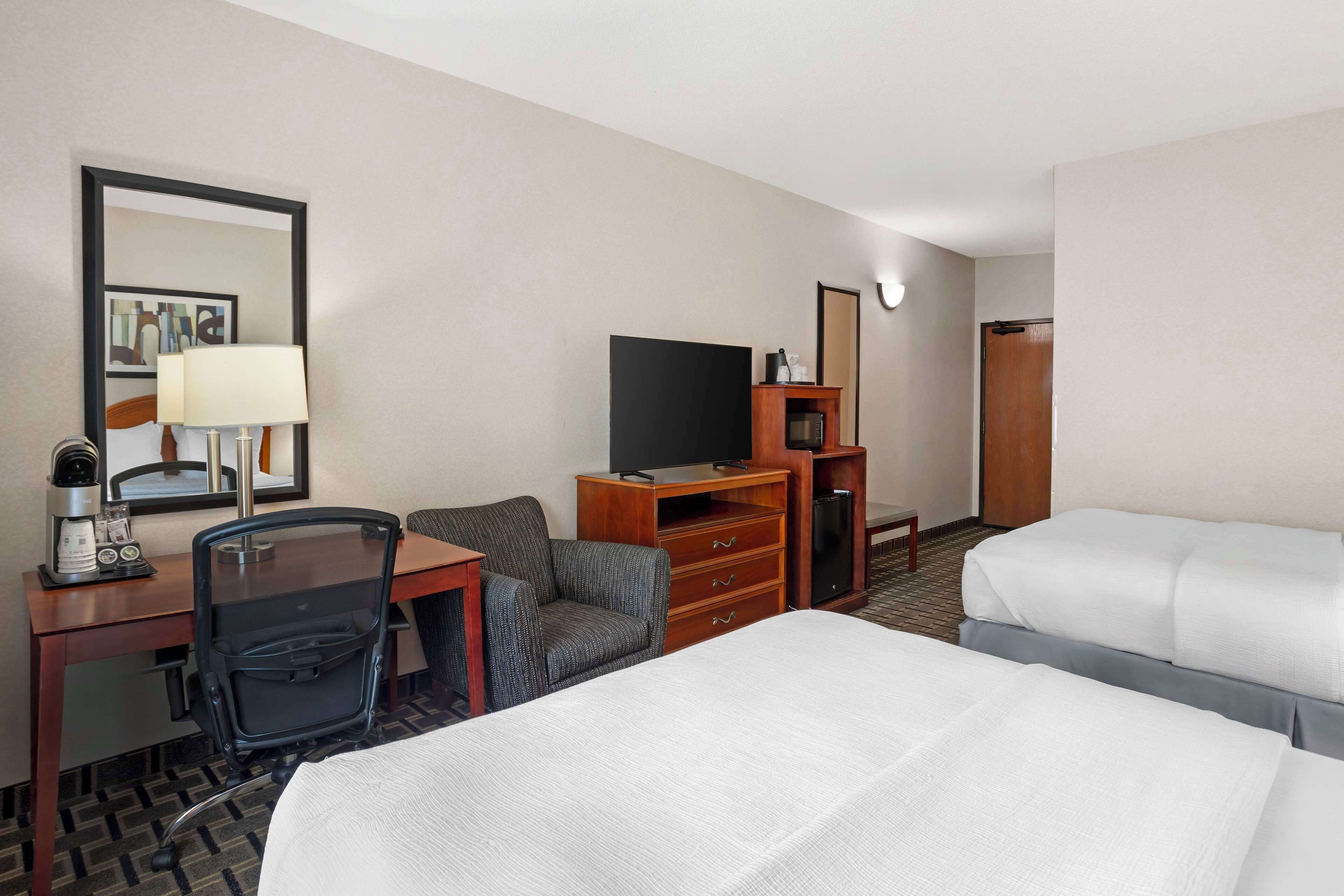 Una habitación de hotel con una cama, un escritorio con lámpara, una silla, un televisor y un aparador.