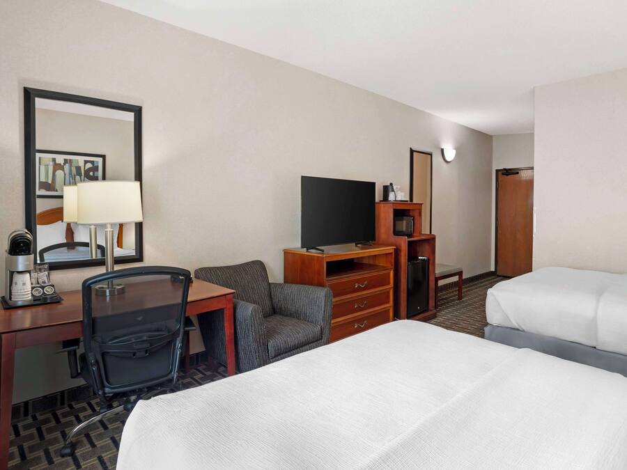 Una habitación de hotel con una cama, un escritorio con lámpara, una silla, un televisor y un aparador.