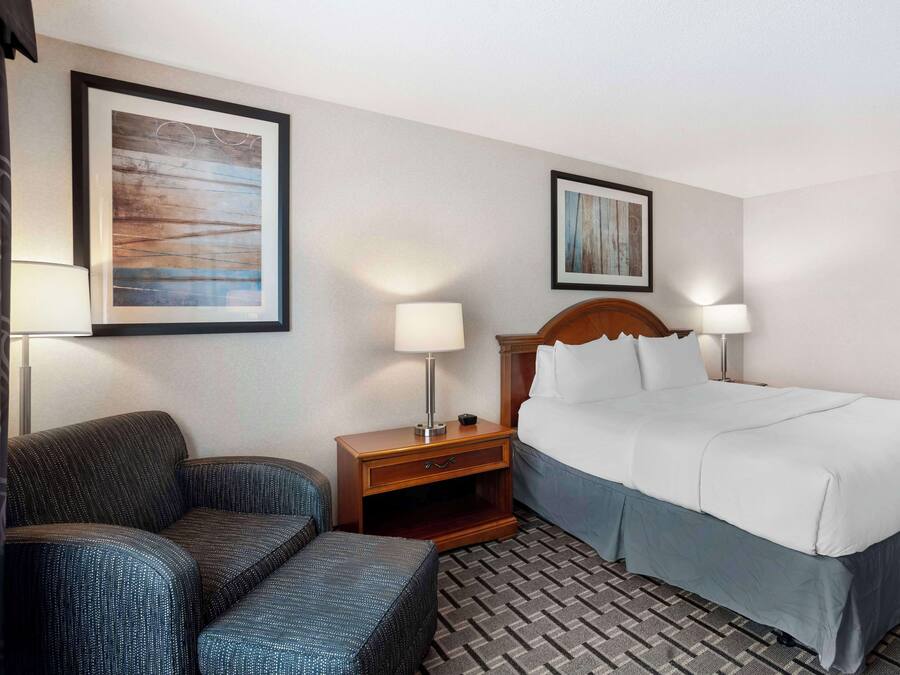 Een hotelkamer met een bed, twee bedlampen, een stoel en twee kunstwerken in lijsten aan de muur.