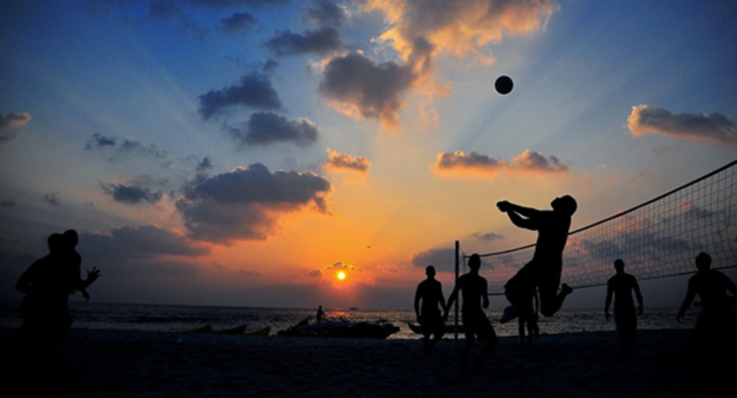 Silhouettes of people playing beach volleyball at sunset.