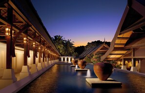 A serene hotel corridor with a reflective pool, traditional architecture, and ambient lighting.