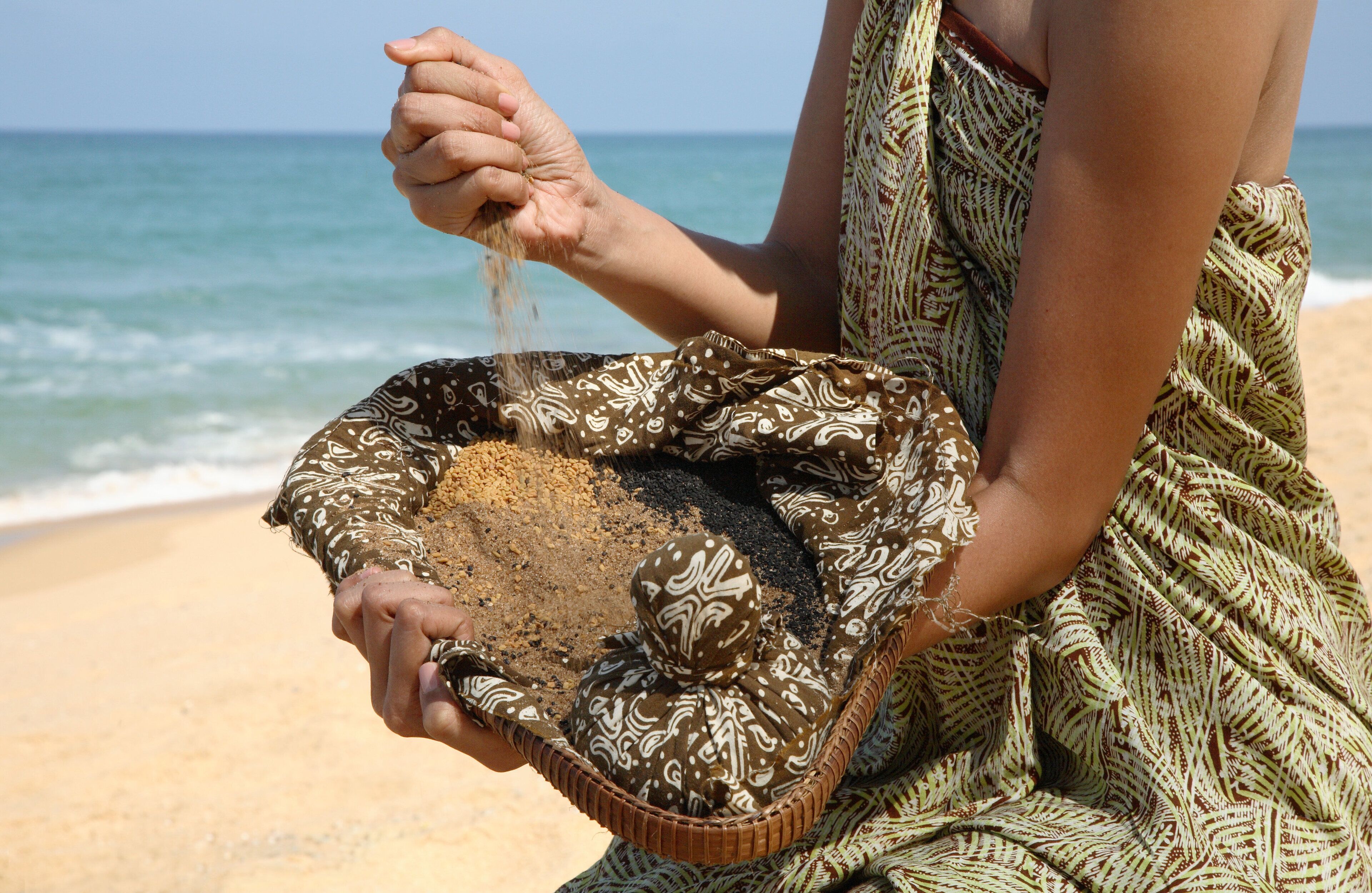 Une personne tenant un panier tressé rempli de sable sur une plage.