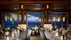 Een restaurant met gedekte tafels, met uitzicht op de zee bij zonsondergang.