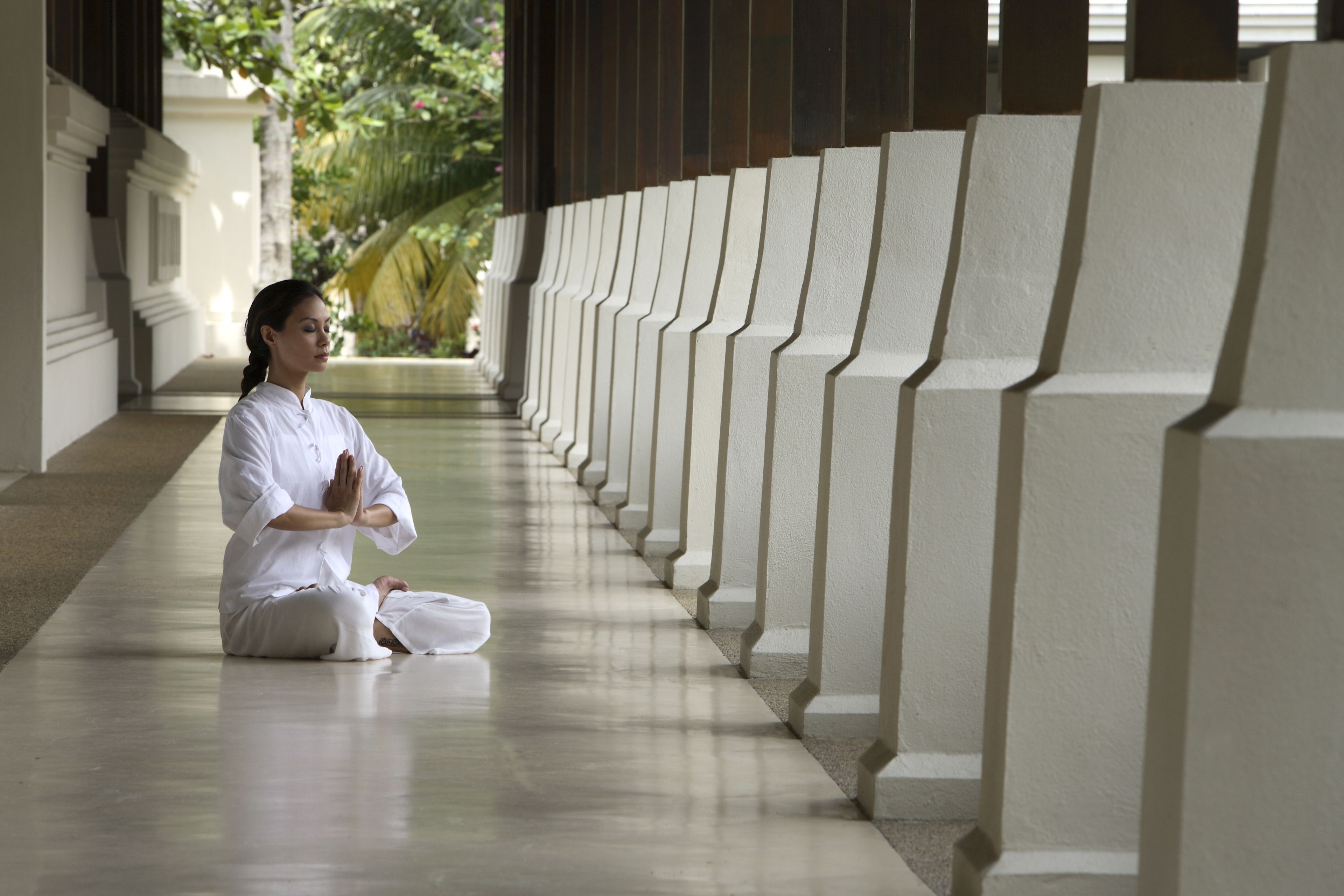 A person sitting in a meditative pose in a corridor with a series of columns.