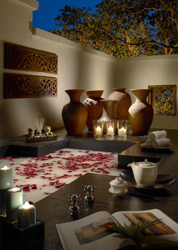 A serene outdoor relaxation area with large vases, candles, and a water feature with rose petals.