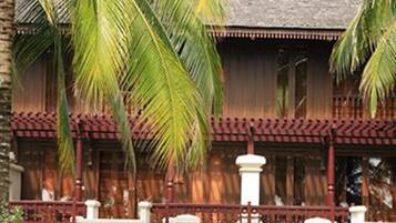 A traditional wooden building with a balcony, palm trees, and two lounge chairs with people relaxing.