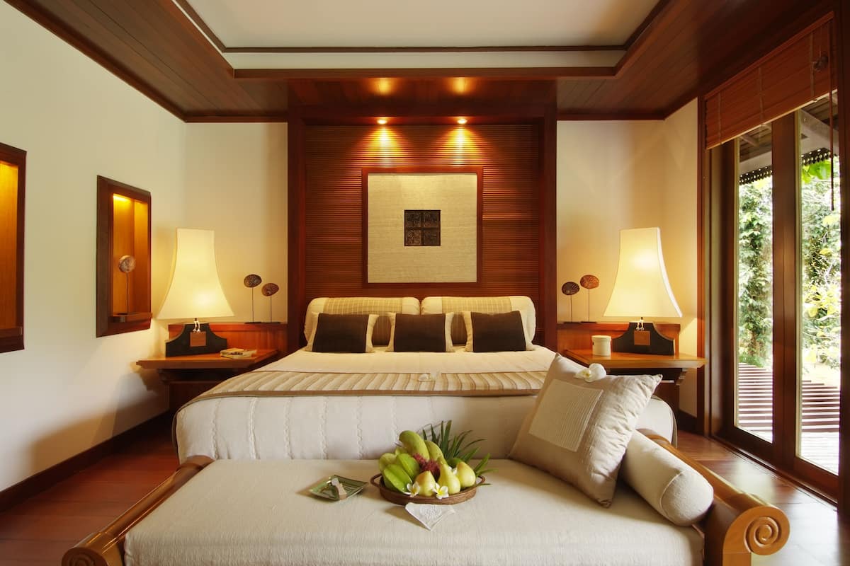 A hotel room with a large bed, two bedside lamps, a wooden headboard, and a window with a view of greenery.