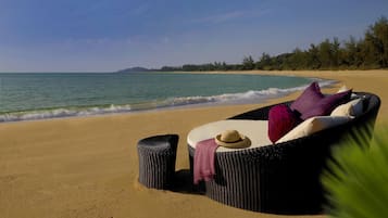 Una poltrona in vimini con cuscini e un cappello di paglia su una spiaggia sabbiosa con onde dell'oceano.