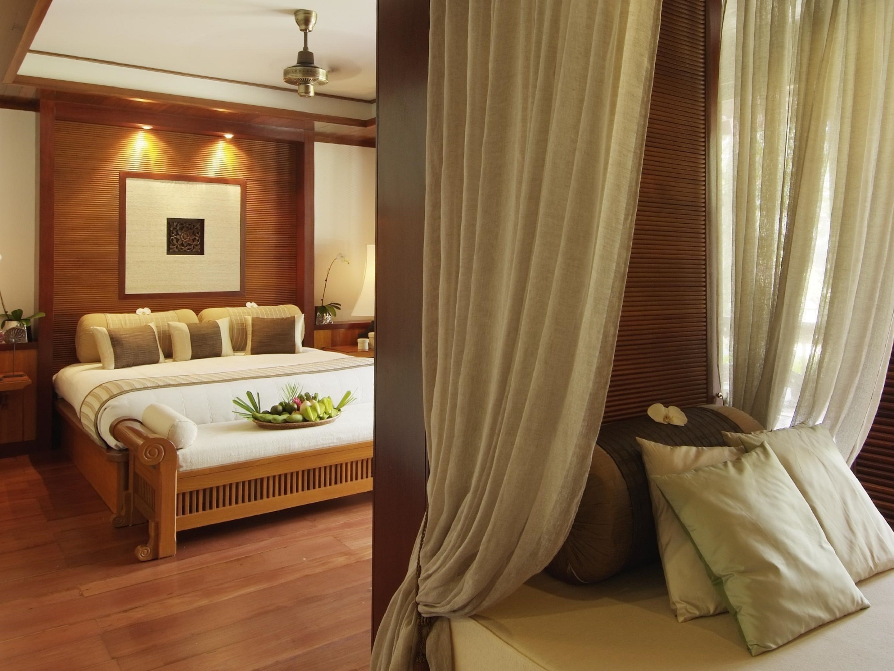 A bedroom with a wooden bed frame, a bedside table, a nightstand, a ceiling fan, and a wall-mounted picture.