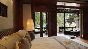A bedroom with a large bed, a sitting area with a table and chairs, and a view of the garden.
