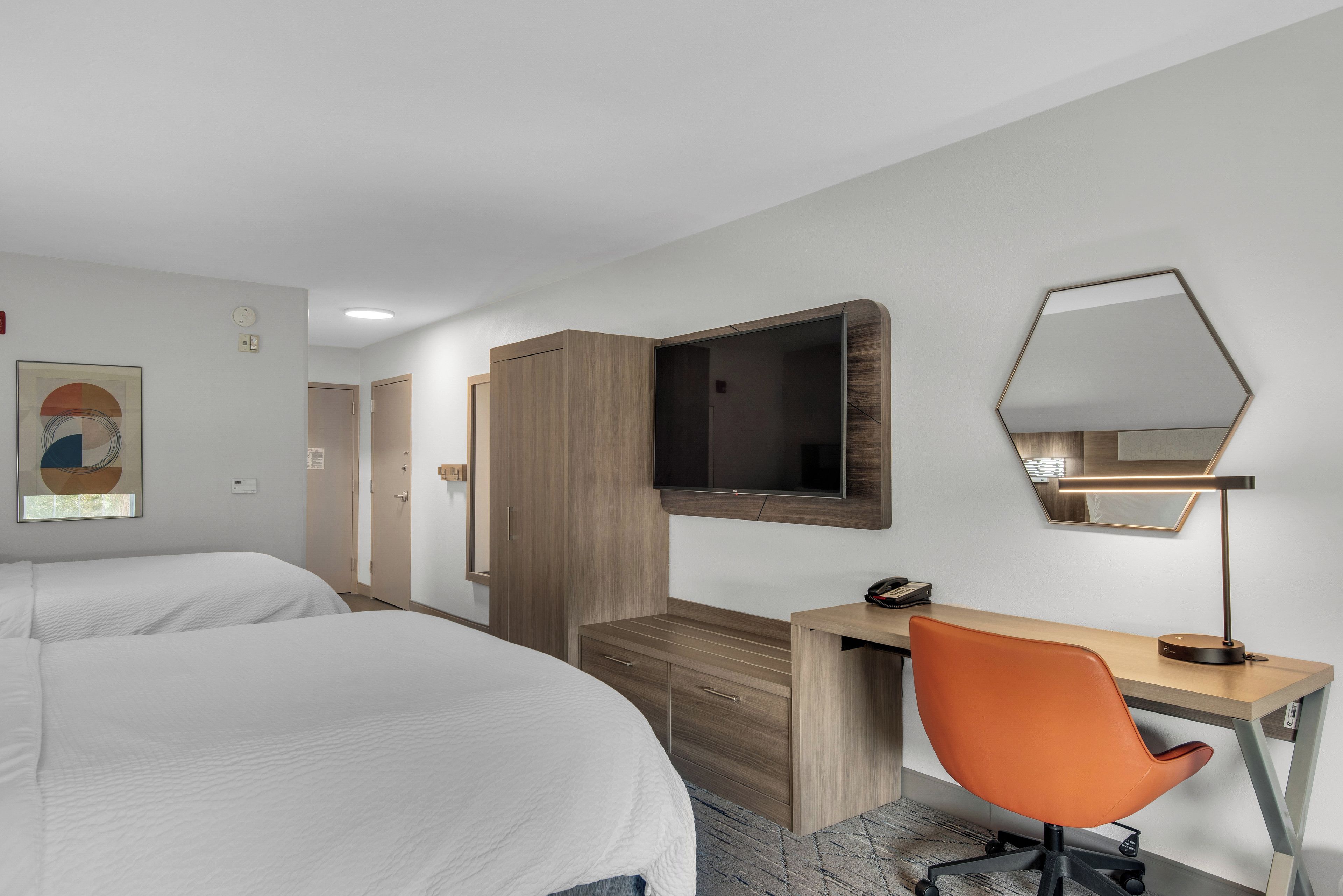 Une chambre d’hôtel avec deux lits, un bureau, une chaise, une télévision et un miroir.